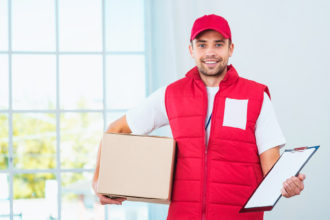 Delivery service worker in uniform delivering parcel. Man with box holding document to sign and looking at camera